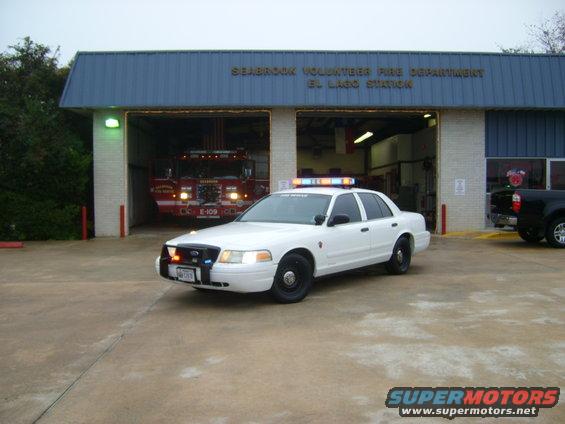 White police car parked in front of Seabrook Volunteer Fire Department El Lago Station, with a fire truck visible inside one bay