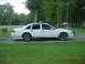 2003 Ford Crown Victoria - A white sedan is parked on a paved surface with a grassy area in front and trees in the background.