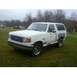 1989 Ford Bronco - This white Ford Bronco is parked outside on a cloudy day with trees in the background.