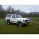 1989 Ford Bronco - This white Ford Bronco is parked outside on a cloudy day with trees in the background.