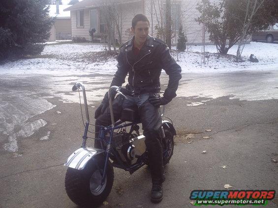 Blue mini bike with chrome fenders and a man in a leather jacket sitting on it