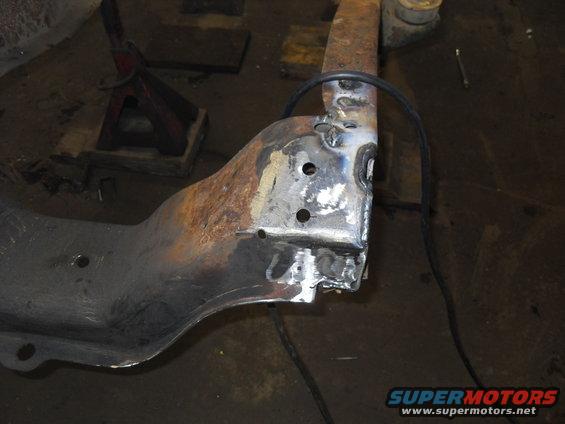 Close-up of a rusty metal frame section with fresh welds and drilled holes