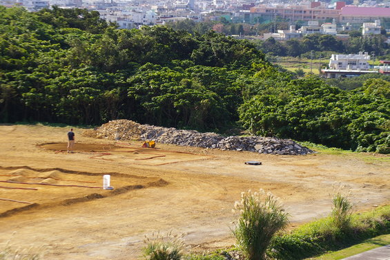 Construction site with dirt mounds, piles of rocks, a person, and a small yellow construction vehicle