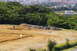 1986 Ford Bronco - A wide view of a construction site with a person and equipment, set against a backdrop of lush green trees and distant buildings.