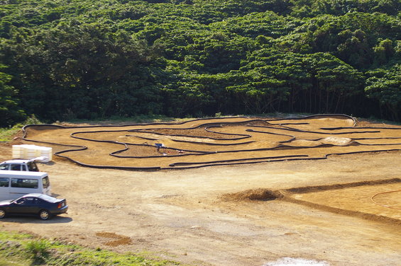 RC car track with a white van and a dark sedan parked on dirt