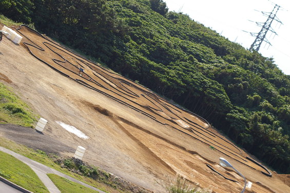 RC car track winding up a grassy and dirt hillside with trees and a power line tower