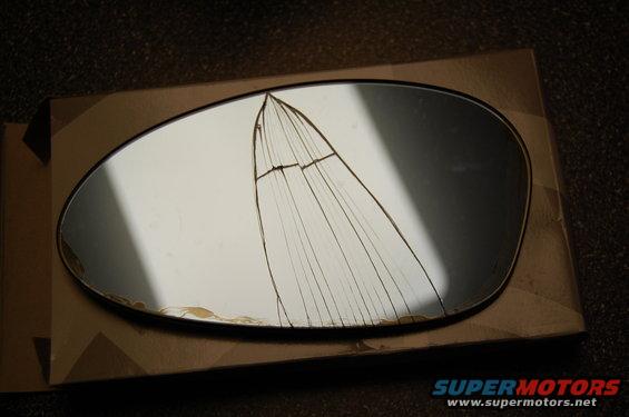 Cracked side mirror glass on a cardboard box. Text 'SUPERMOTORS' visible