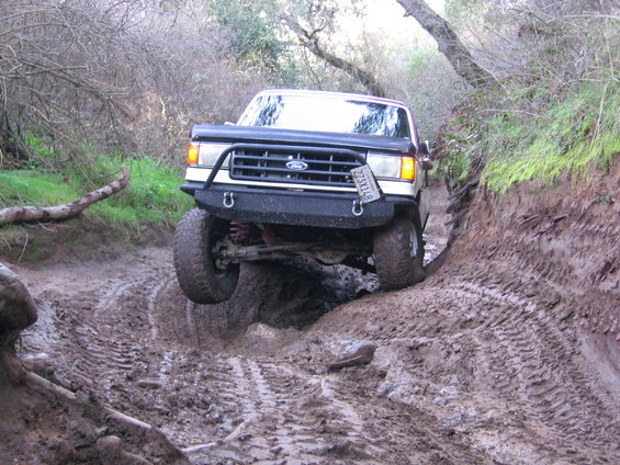 Ford Bronco with aftermarket bumper navigating a muddy rut, front wheel off the ground