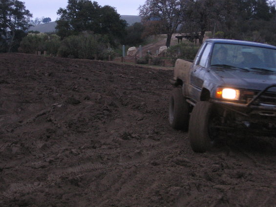 Dark pickup truck with headlights on driving through mud