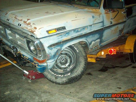 Ford truck on trailer, front fender rust, blue and white paint, jack under wheel