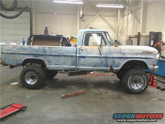 1971 Ford F-100 pickup truck with lifted suspension and aftermarket wheels, in a workshop