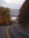 1968 Ford Mustang - A scenic autumn drive unfolds on a winding road, with colorful foliage framing a view of a lake and rolling hills.