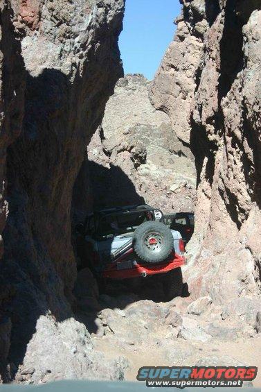 Two off-road vehicles wedged between narrow rock formations on a trail
