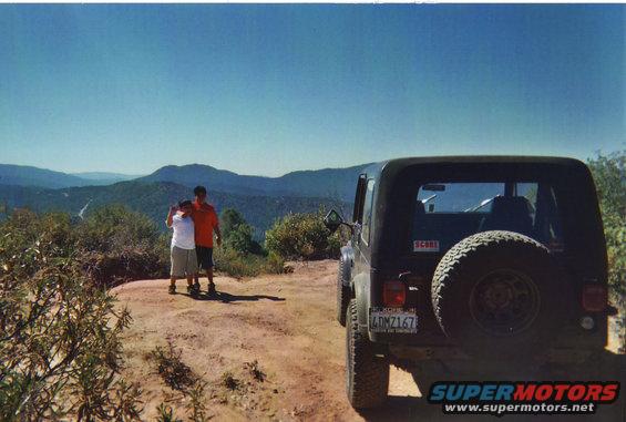 Black Jeep CJ-7 with spare tire on rear, parked on dirt road with mountain view