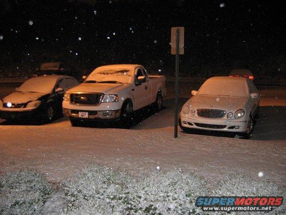 White Ford F-150 pickup truck parked in snow at night, next to a sedan and a Mercedes
