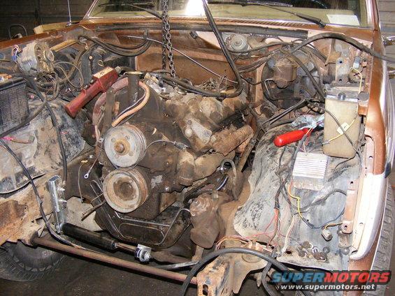 Brown 1985 Ford Bronco engine bay with engine removed, showing rusty components and wiring