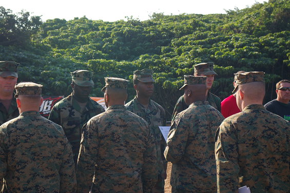 Marines in camouflage uniforms gathered outdoors with trees in the background