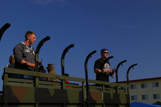 Camouflage military truck bed with two men standing, one holding a remote control