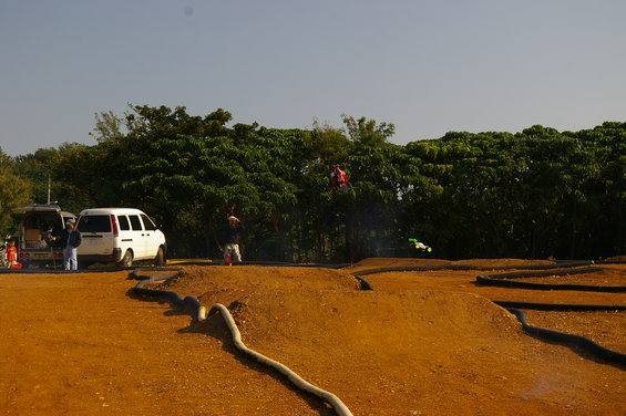 Two white vans parked near a remote control race track with trees in the background
