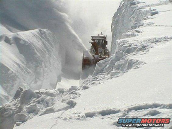 Snow blower clearing a path through deep snow, viewed from the side