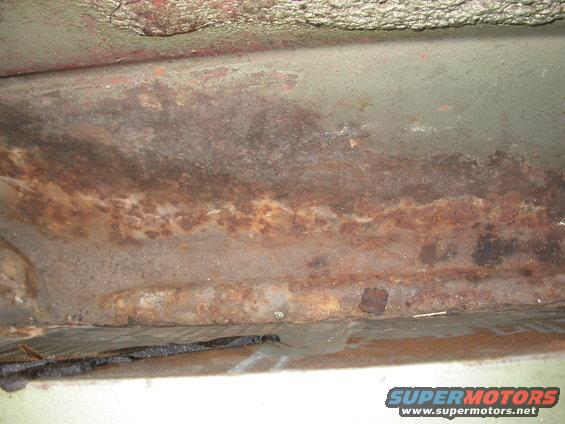 close-up of rusted metal on a car's undercarriage, showing significant corrosion and wear