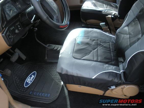 1990 Ford Bronco interior showing dashboard, steering wheel, floor mats with Ford logo, and seat covers