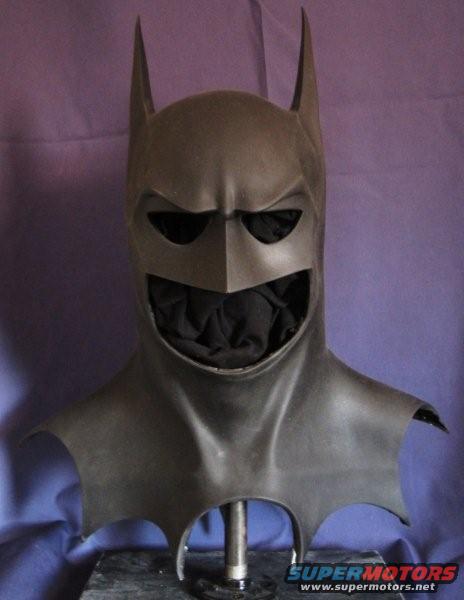 Batman cowl with pointed ears and menacing grin, displayed on a stand