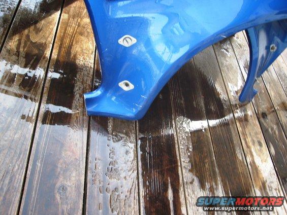 Blue fender section with mounting holes on wet wooden planks