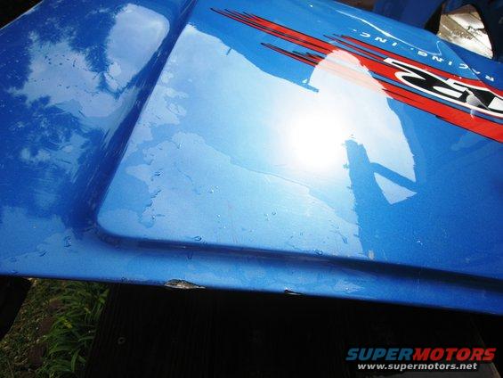 blue car fender with red and black racing stripes and "RACING INC." text. Some water droplets on surface
