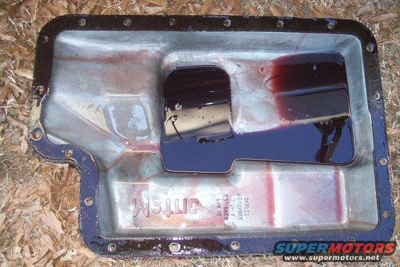 Transmission pan with dark fluid and some residue. Text is visible on the pan