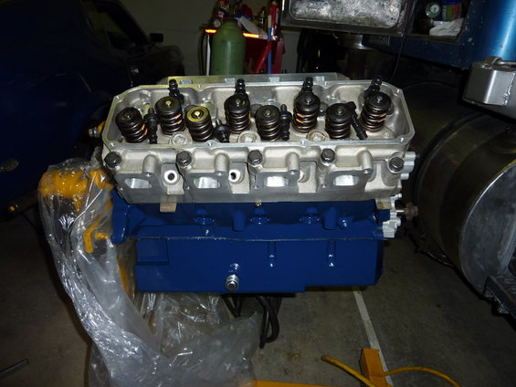 engine block painted blue with silver cylinder head on top, in a garage setting