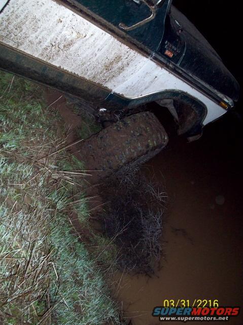Muddy off-road vehicle with one tire deep in mud and water