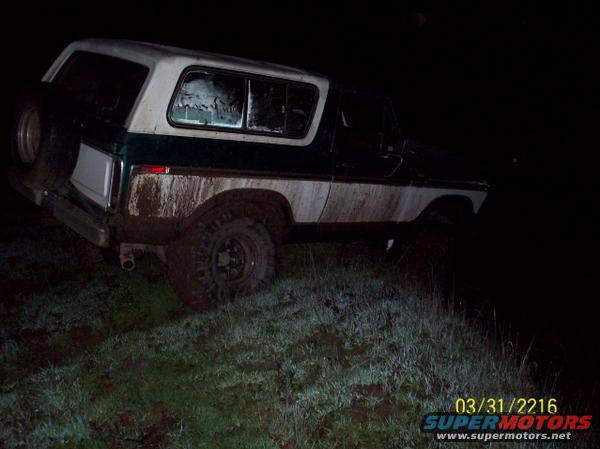 1979 Ford Bronco parked on grassy incline at night, covered in mud