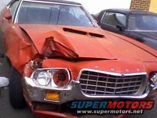 Damaged red 1970 Ford Torino front end with grille and hood crumpled, parked next to a black car