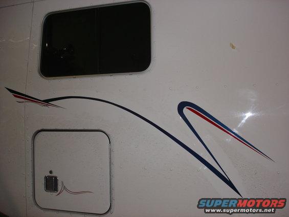 Side panel of a white truck with a dark window and blue/red/black graphics. Includes a storage compartment door