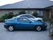 1993 Mazda MX-3 - A blue 1993 Mazda MX-3 coupe is parked next to a silver sedan in front of a house.