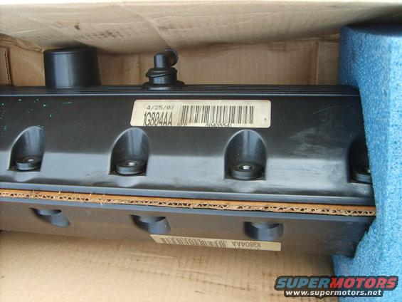 Black valve cover with a "4/25/01 1G804AA" label, packed in a cardboard box with foam