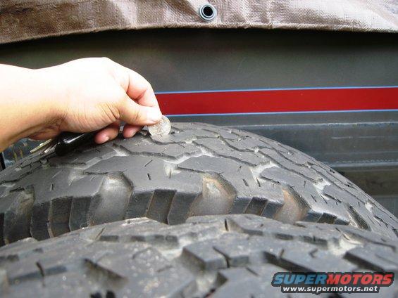 Tire tread with a coin for scale, showing wear. A red stripe is visible on the vehicle body