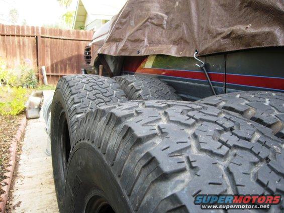 Close-up of off-road tires in front of a covered vehicle with red and blue stripes on its side