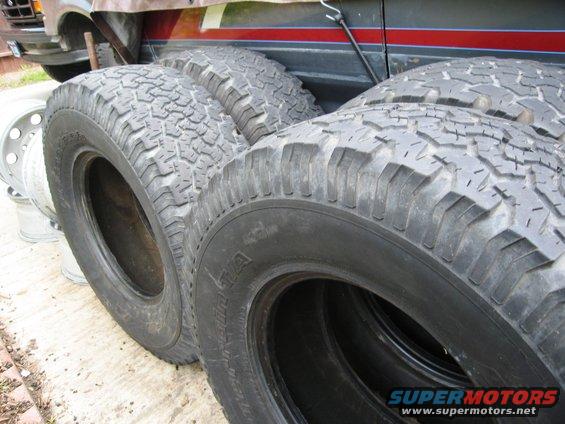Several off-road tires stacked up, with a vehicle in the background