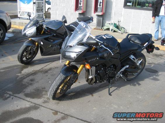 Two sport motorcycles parked outside a building. One is black with gold forks, the other is dark gray