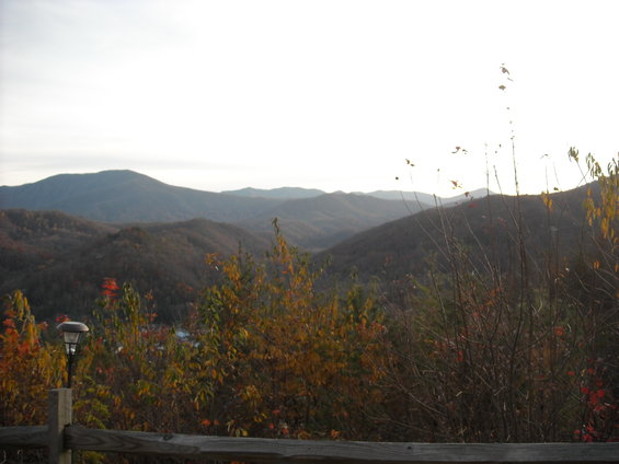 Mountain range under a bright sky, with autumn foliage in the foreground and a wooden fence