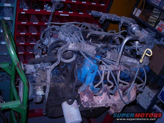 Engine assembly with blue intake manifold and rusted exhaust manifolds, mounted on a green stand
