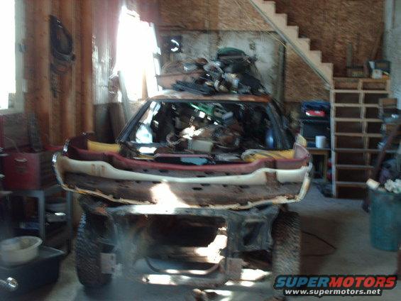 Car body with front end removed, sitting on tires in a garage