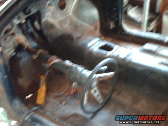 Interior of a car with no seats, showing the floor pan and steering column