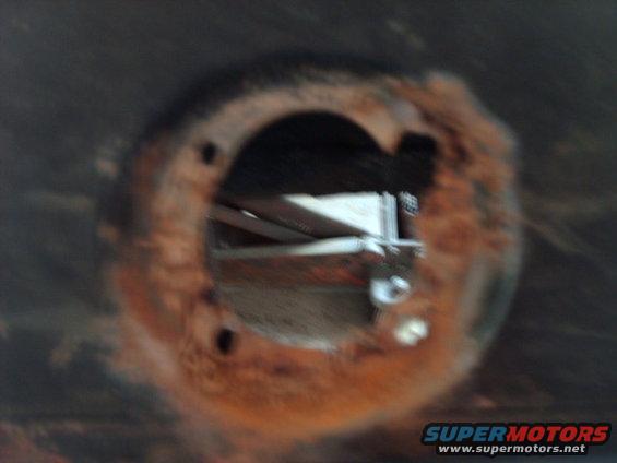 close-up of a rusted circular opening on a vehicle's undercarriage, showing some internal bracing