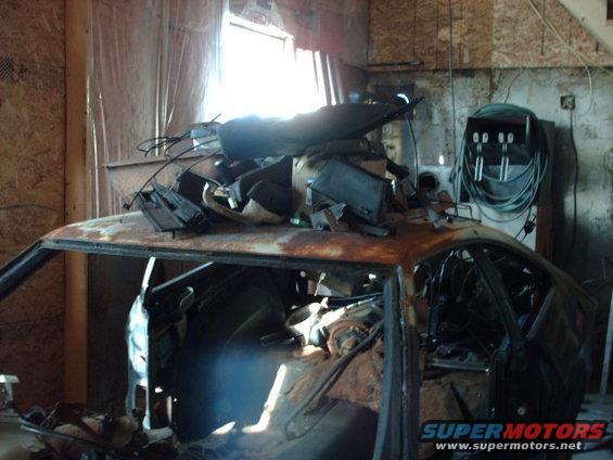 Rusted car body, stripped and filled with parts, viewed from the side in a workshop