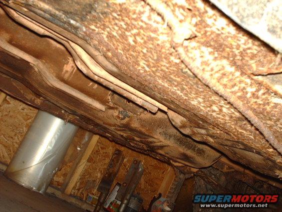 Heavily rusted undercarriage of a vehicle, showing frame rails and exhaust components