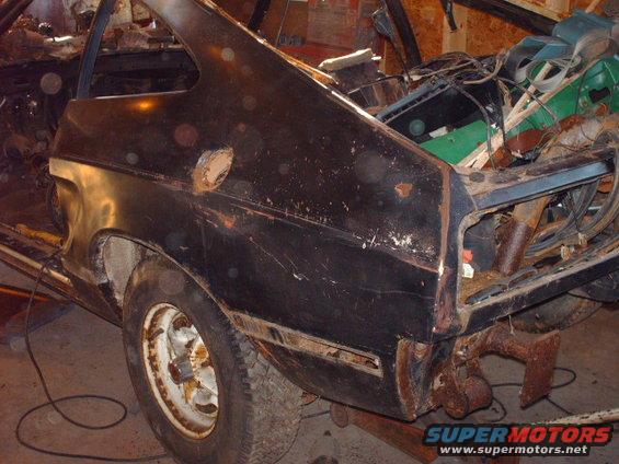 Black car rear quarter panel with rust and damage, viewed from the rear