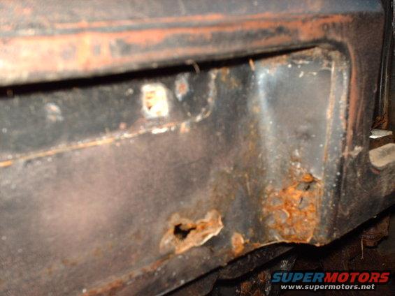 Close-up of rusted metal with holes, showing corrosion on a vehicle part